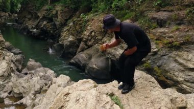 Bir maceracı nehir kıyısında etrafındaki eşsiz antik kayalarla sıcak baharat çayının tadını çıkarıyor. Antik nehir kıyısında sıcak çay içen Asyalı bir gezgin.