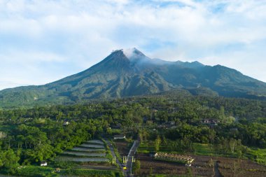 Aerial view of a volcano in the morning with a view of the forest and a branching road in front. Drone photo shows the beauty of Mount Merapi in Sleman, Yogyakarta, Indonesia at sunrise