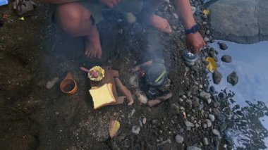 Güzel bir nehir kıyısında su kaynatmak için odundan ateş yakan erkek bir maceracının ellerine yakından bakın. Bushcraft yemek konsepti nehir kıyısında basit ekipmanlarla gezen bir erkek gezgin.