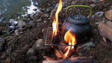 Güzel bir nehir kıyısında su kaynatmak için odundan ateş yakan erkek bir maceracının ellerine yakından bakın. Bushcraft yemek konsepti nehir kıyısında basit ekipmanlarla gezen bir erkek gezgin.
