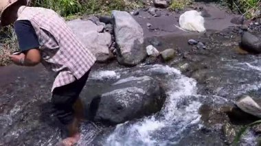 Asyalı bir adam nehirde doğanın huzurunun tadını çıkarmak için kayaların üzerinden geçerek nehri geçer. Maceraperest bir adam, temiz bir nehirde kayaların üzerinde bir fincan kahvenin tadını çıkarır..