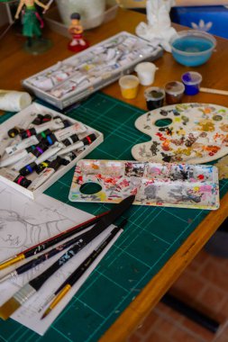 O kadar sık kullanılan bir boya paleti ki, kullanılan boya birbiri ardına kurumuş ve üst üste yığılmış. Bir boya paleti ve masaya saçılmış diğer resim malzemelerinin yakın çekimi.