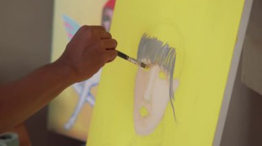 Fırça kullanarak tuvale parlak renkler uygulayan bir sanatçı. Bir ressamın bir kızın yüzünü pop tarzında boyama işleminden fırça darbelerine yakın çekim