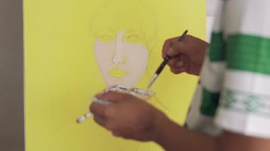 Fırça kullanarak tuvale parlak renkler uygulayan bir sanatçı. Bir ressamın bir kızın yüzünü pop tarzında boyama işleminden fırça darbelerine yakın çekim