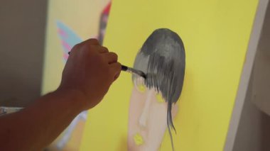 Fırça kullanarak tuvale parlak renkler uygulayan bir sanatçı. Bir ressamın bir kızın yüzünü pop tarzında boyama işleminden fırça darbelerine yakın çekim