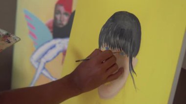 Fırça kullanarak tuvale parlak renkler uygulayan bir sanatçı. Bir ressamın bir kızın yüzünü pop tarzında boyama işleminden fırça darbelerine yakın çekim