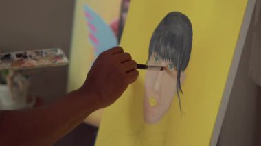 Fırça kullanarak tuvale parlak renkler uygulayan bir sanatçı. Bir ressamın bir kızın yüzünü pop tarzında boyama işleminden fırça darbelerine yakın çekim