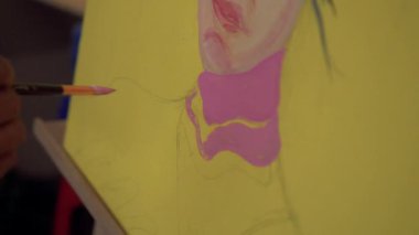 Fırça kullanarak tuvale parlak renkler uygulayan bir sanatçı. Bir ressamın bir kızın yüzünü pop tarzında boyama işleminden fırça darbelerine yakın çekim