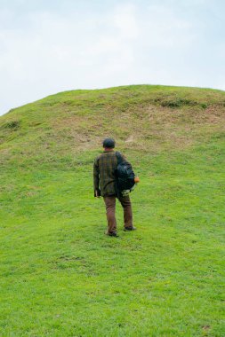 Erkek bir maceracı yeşil çimenlerin engin güzelliğinin tadını çıkarıyor. Asyalı erkek gezgin rahatlar ve temiz ve güzel yeşil tepelerin doğal cazibesine hayran kalır..