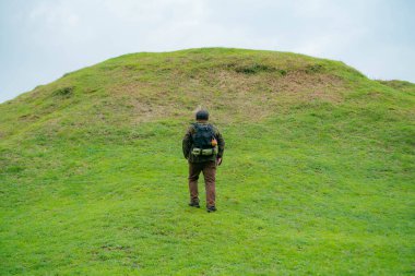Erkek bir maceracı yeşil çimenlerin engin güzelliğinin tadını çıkarıyor. Asyalı erkek gezgin rahatlar ve temiz ve güzel yeşil tepelerin doğal cazibesine hayran kalır..