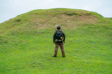 Erkek bir maceracı yeşil çimenlerin engin güzelliğinin tadını çıkarıyor. Asyalı erkek gezgin rahatlar ve temiz ve güzel yeşil tepelerin doğal cazibesine hayran kalır..