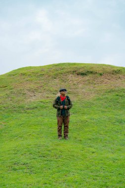 Erkek bir maceracı yeşil çimenlerin engin güzelliğinin tadını çıkarıyor. Asyalı erkek gezgin rahatlar ve temiz ve güzel yeşil tepelerin doğal cazibesine hayran kalır..
