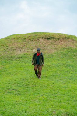 Erkek bir maceracı yeşil çimenlerin engin güzelliğinin tadını çıkarıyor. Asyalı erkek gezgin rahatlar ve temiz ve güzel yeşil tepelerin doğal cazibesine hayran kalır..