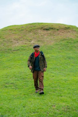 Erkek bir maceracı yeşil çimenlerin engin güzelliğinin tadını çıkarıyor. Asyalı erkek gezgin rahatlar ve temiz ve güzel yeşil tepelerin doğal cazibesine hayran kalır..