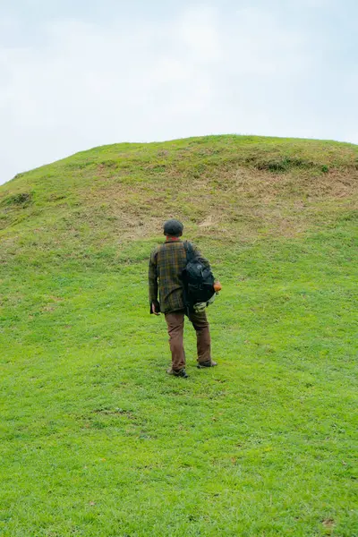 Erkek bir maceracı yeşil çimenlerin engin güzelliğinin tadını çıkarıyor. Asyalı erkek gezgin rahatlar ve temiz ve güzel yeşil tepelerin doğal cazibesine hayran kalır..