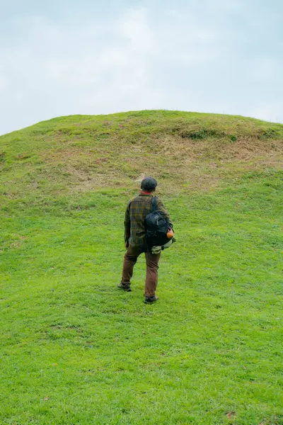 Erkek bir maceracı yeşil çimenlerin engin güzelliğinin tadını çıkarıyor. Asyalı erkek gezgin rahatlar ve temiz ve güzel yeşil tepelerin doğal cazibesine hayran kalır..