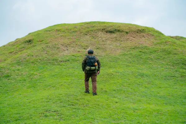 Erkek bir maceracı yeşil çimenlerin engin güzelliğinin tadını çıkarıyor. Asyalı erkek gezgin rahatlar ve temiz ve güzel yeşil tepelerin doğal cazibesine hayran kalır..