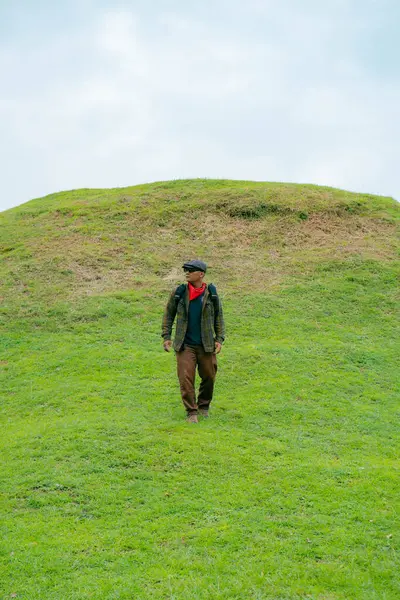 Erkek bir maceracı yeşil çimenlerin engin güzelliğinin tadını çıkarıyor. Asyalı erkek gezgin rahatlar ve temiz ve güzel yeşil tepelerin doğal cazibesine hayran kalır..