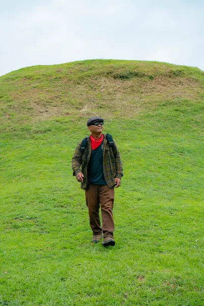 Erkek bir maceracı yeşil çimenlerin engin güzelliğinin tadını çıkarıyor. Asyalı erkek gezgin rahatlar ve temiz ve güzel yeşil tepelerin doğal cazibesine hayran kalır..
