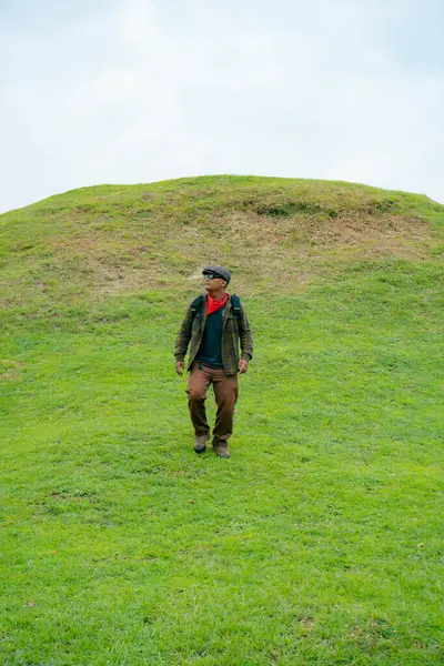 Erkek bir maceracı yeşil çimenlerin engin güzelliğinin tadını çıkarıyor. Asyalı erkek gezgin rahatlar ve temiz ve güzel yeşil tepelerin doğal cazibesine hayran kalır..