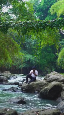 Asyalı bir adam İrlanda 'da geleneksel bir enstrüman çalıyor. Adı da yemyeşil bir nehir kıyısında teneke düdük. Bir teneke ıslık çalan, yeşil ağaçlarla çevrili nehir kenarındaki büyük bir kayanın üzerinde yeteneklerini sergiliyor..