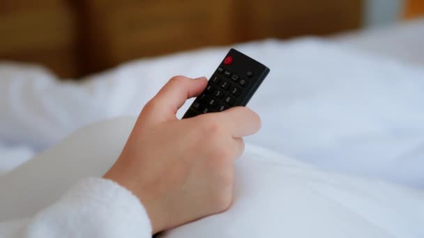 一个看电视的女孩床白色的床 在旅馆房间里度假 一个女孩用遥控器开关电视机 电视遥控装置 遥控装置高质量的4K镜头 — 图库视频影像