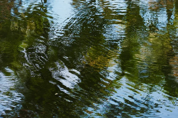 stock image The tranquil scene of the pond is artfully captured by the shimmering water as it mirrors both the sky and the trees' shade. Abstract background from reflections on the water surface.