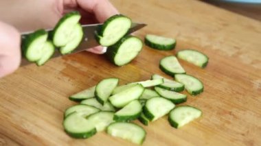 Bir kız, ahşap kaplama üzerinde bir bıçakla salatalık kesiyor.