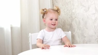 Beyaz tişörtlü küçük bir kız masaya oturur ve büyük bir portakalla oynar.