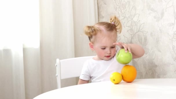 一个穿着白色T恤的小女孩坐在桌旁玩水果游戏 橙子和苹果 — 图库视频影像