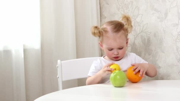 一个穿着白色T恤的小女孩坐在桌旁玩水果游戏 橙子和苹果 — 图库视频影像