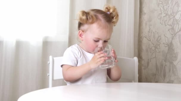 一个穿着白色T恤的小女孩坐在桌旁 喝着杯子里的水 — 图库视频影像