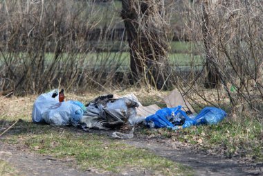 Çevre kirliliği. Ormanda yolda çöp torbaları, nehirde araba tekerlekleri ve kırsal alandaki eski mobilyalar var..