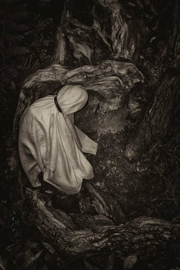 Beyaz bir battaniyeye sarılı bir insanın monokromatik görüntüsü doğanın bir arka planına karşı..