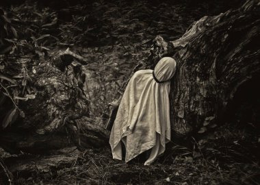 Beyaz bir battaniyeye sarılı bir insanın monokromatik görüntüsü doğanın bir arka planına karşı..