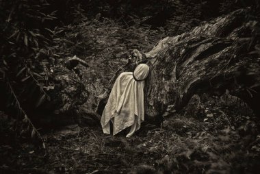 Beyaz bir battaniyeye sarılı bir insanın monokromatik görüntüsü doğanın bir arka planına karşı..