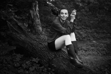 Bahar ormanında poz veren lastik çizmeli bir kız, çiçek açan ağaçlar ve canlı yeşilliklerle çevrili, doğanın yenilenmesinin özünü yayıyor..