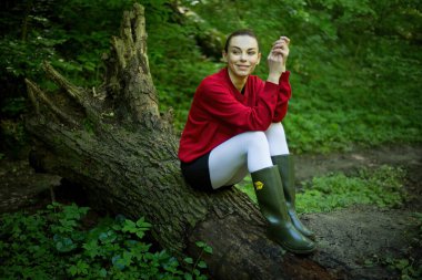 Bahar ormanında poz veren lastik çizmeli bir kız, çiçek açan ağaçlar ve canlı yeşilliklerle çevrili, doğanın yenilenmesinin özünü yayıyor..