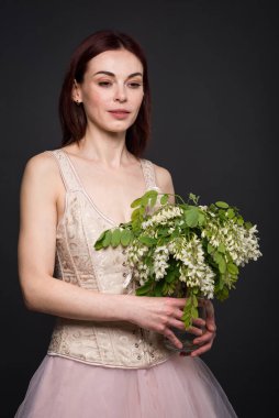 Büyüleyici bir kadın fotoğraf stüdyosunda bir akasya dalıyla poz veriyor..