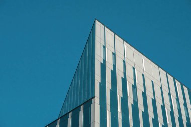 Gökyüzüne karşı modern binaların parçaları, parlak çizgiler, cam yansımalar ve kalın mimari detaylar yakalıyor, kentsel tasarımı ufkun açık genişliğiyle harmanlıyor..