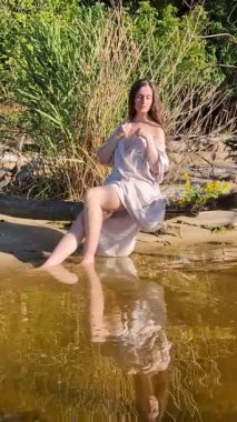 Kafasında çelenk olan uzun beyaz elbiseli bir kız nehir kıyısında yürüyor.