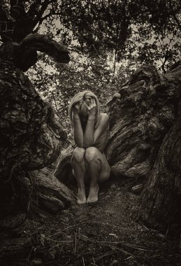 Kadın ağaç kökleri arasında cenin pozisyonunda, doğa ve yeniden doğuşu sembolize ediyor..