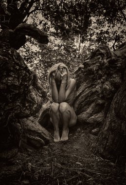Kadın ağaç kökleri arasında cenin pozisyonunda, doğa ve yeniden doğuşu sembolize ediyor..