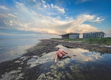 Suda çıplak figür, bulutlu gökyüzü, kırsal kıyı, siyah ve beyaz.