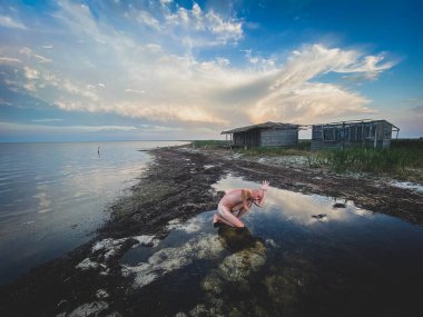 Suda çıplak figür, bulutlu gökyüzü, kırsal kıyı, siyah ve beyaz.