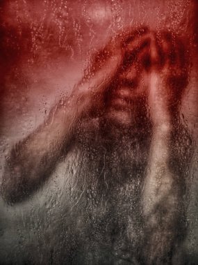 Islak camın arkasında bir adam, elleri üzerine bastırılmış, duygusal acı ifade ediyor..