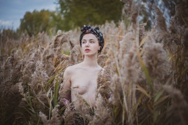 Sonbahar günbatımında nehir kamışlarının arasında üstsüz bir kadın duruyor..