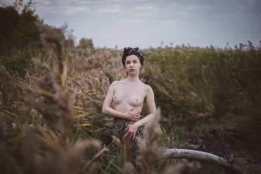 Sonbahar günbatımında nehir kamışlarının arasında üstsüz bir kadın duruyor..