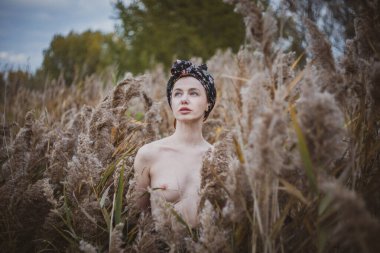 Sonbahar günbatımında nehir kamışlarının arasında üstsüz bir kadın duruyor..