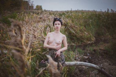 Sonbahar günbatımında nehir kamışlarının arasında üstsüz bir kadın duruyor..